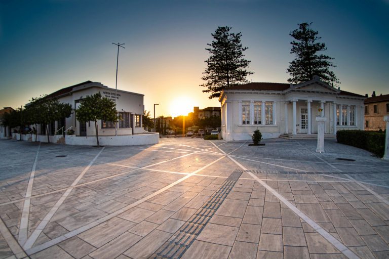 Cypriot buildings with bright facades and a picturesque square in the foreground at sunset.